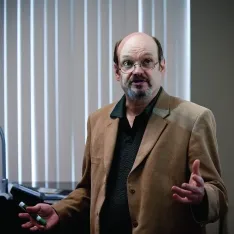 A man in a suit standing in front of a projector screen, delivering a presentation to an audience.